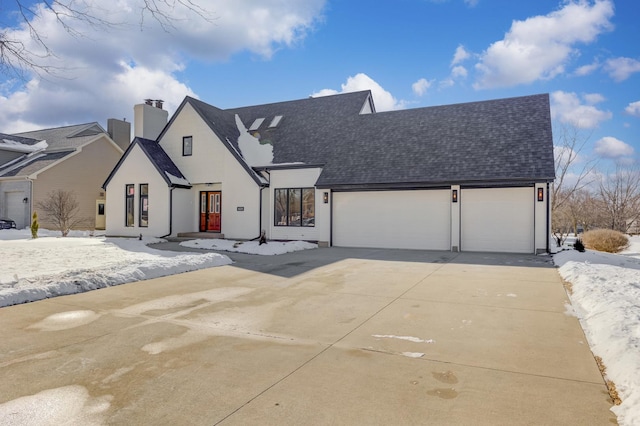 view of front facade with driveway, a garage, a chimney, roof with shingles, and stucco siding