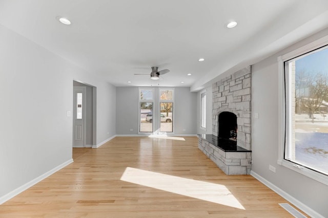 unfurnished living room featuring a wealth of natural light, baseboards, a fireplace, and light wood finished floors