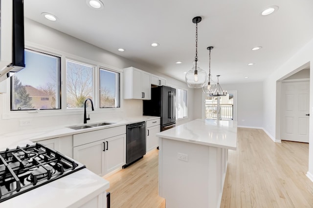 kitchen with white cabinets, a kitchen island, decorative light fixtures, black appliances, and a sink