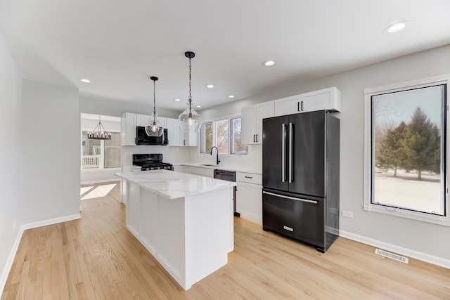 kitchen with a center island, hanging light fixtures, light stone countertops, black appliances, and white cabinetry