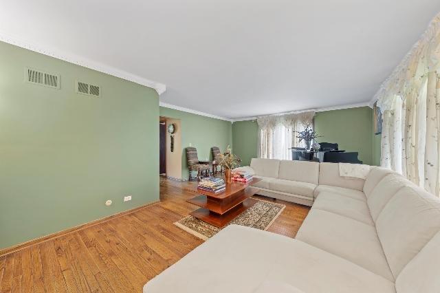 living area with wood finished floors, visible vents, and crown molding