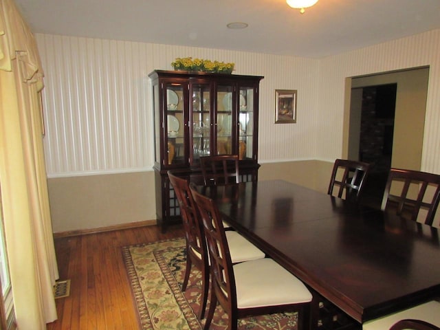 dining area with baseboards, visible vents, wallpapered walls, and wood finished floors