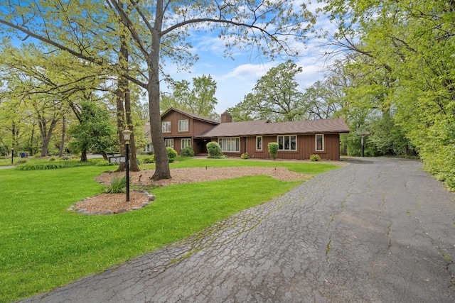 view of front of home with driveway, a chimney, and a front yard