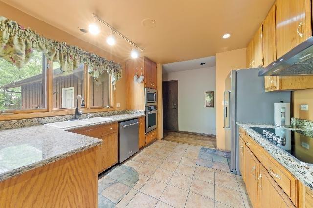 kitchen featuring light tile patterned floors, under cabinet range hood, a sink, appliances with stainless steel finishes, and brown cabinetry