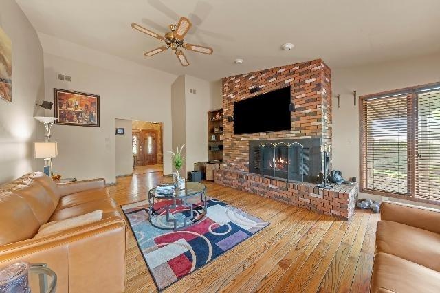 living area featuring a ceiling fan, a fireplace, visible vents, and wood finished floors