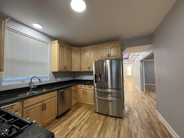 kitchen with baseboards, appliances with stainless steel finishes, dark stone countertops, light wood-type flooring, and a sink