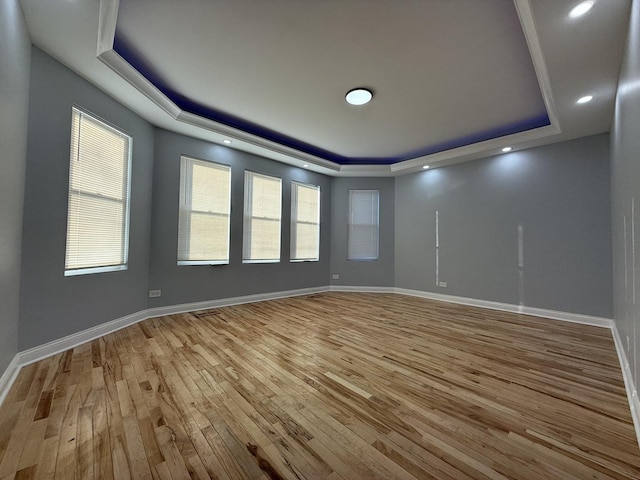 unfurnished room with a tray ceiling, light wood-style flooring, and baseboards