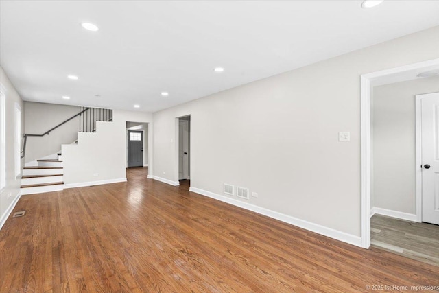 unfurnished living room featuring baseboards, stairs, visible vents, and wood finished floors