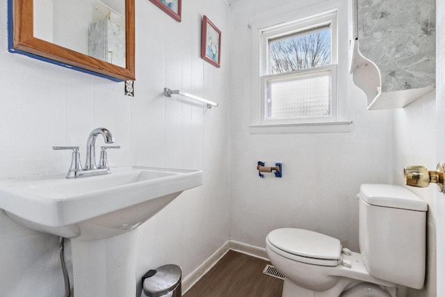 half bath featuring a sink, wood finished floors, toilet, and baseboards