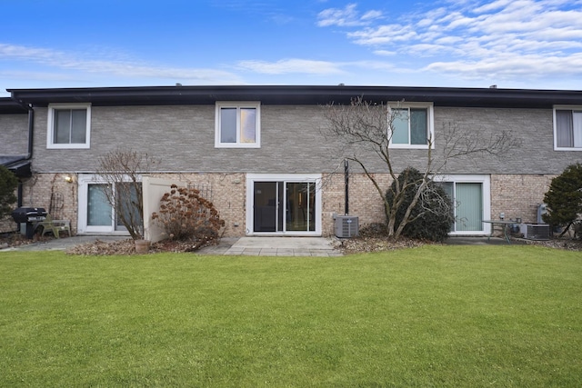 rear view of property with central AC, brick siding, and a lawn