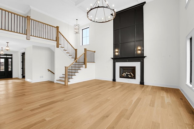 unfurnished living room featuring a towering ceiling, an inviting chandelier, ornamental molding, light wood-type flooring, and stairs