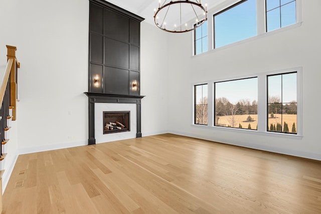 unfurnished living room featuring light wood-style flooring, a large fireplace, baseboards, stairway, and an inviting chandelier