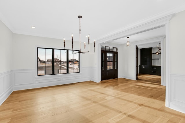 unfurnished dining area featuring a notable chandelier, ornamental molding, a decorative wall, and light wood-style floors