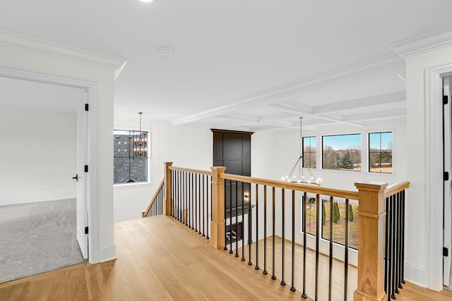 hallway with light wood-style floors, a chandelier, beam ceiling, and an upstairs landing