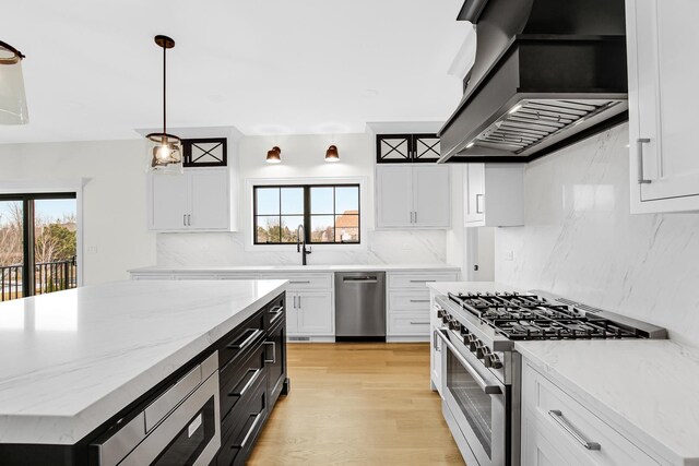 kitchen with wall chimney exhaust hood, a healthy amount of sunlight, white cabinetry, and stainless steel appliances