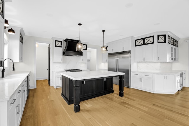 kitchen featuring built in fridge, light wood-style floors, white cabinetry, a sink, and wall chimney range hood