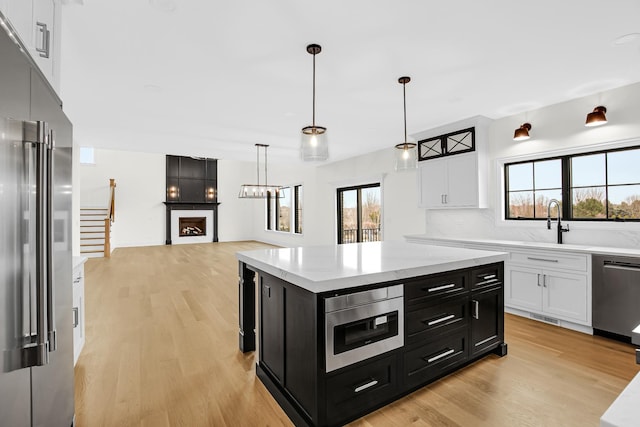 kitchen featuring stainless steel appliances, a large fireplace, white cabinetry, and dark cabinets