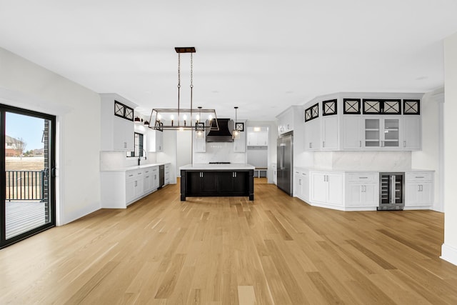 kitchen with light wood finished floors, wine cooler, built in refrigerator, light countertops, and wall chimney range hood