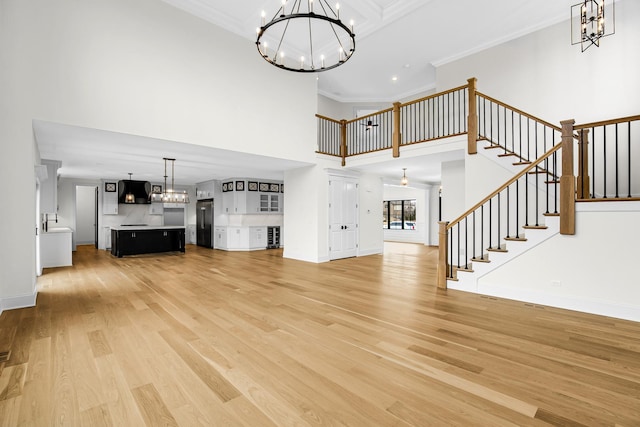 unfurnished living room featuring light wood-style flooring, a high ceiling, stairs, crown molding, and a chandelier