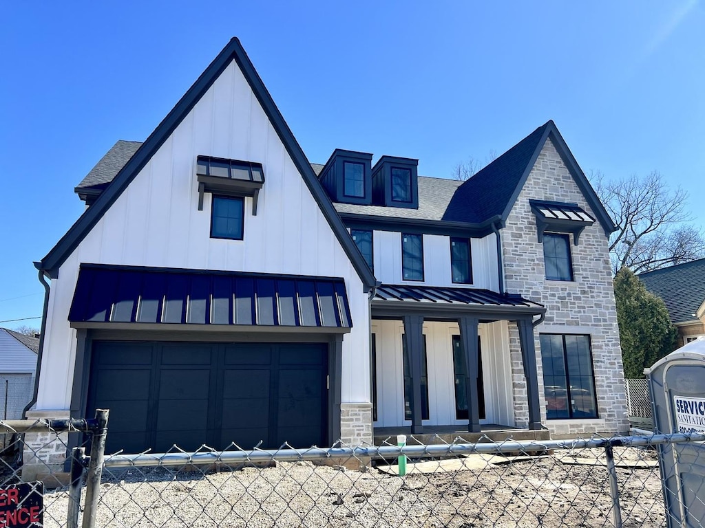 modern farmhouse style home featuring a fenced front yard, a garage, a standing seam roof, and stone siding