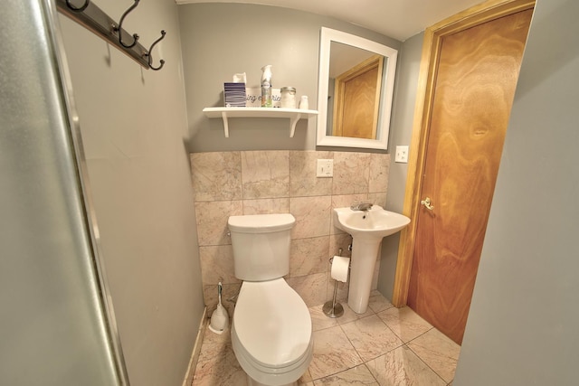 half bathroom featuring toilet, a sink, and tile walls