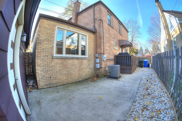 view of side of home with brick siding, a patio, a chimney, cooling unit, and a fenced backyard