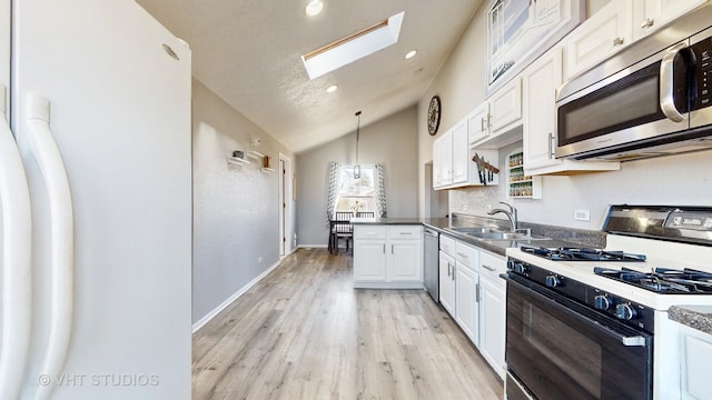 kitchen with stainless steel appliances, a sink, light wood-style floors, white cabinets, and lofted ceiling with skylight