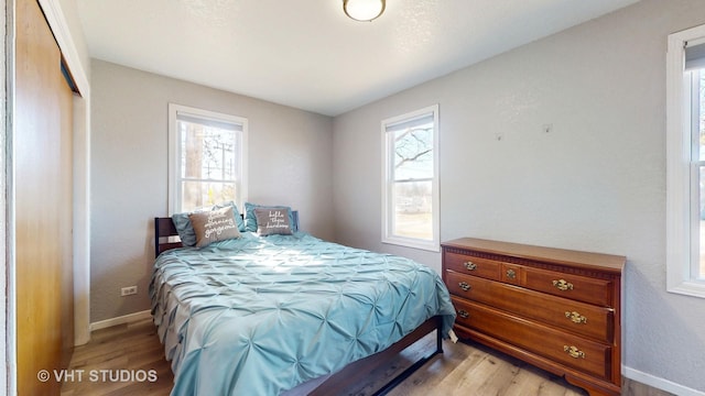 bedroom with a closet, multiple windows, light wood-style flooring, and baseboards