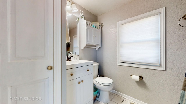 bathroom with a textured wall, toilet, vanity, baseboards, and tile patterned floors