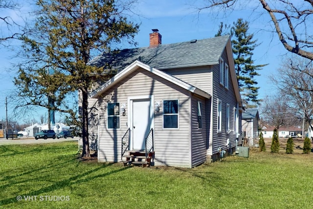 back of property with entry steps, a chimney, a lawn, and roof with shingles