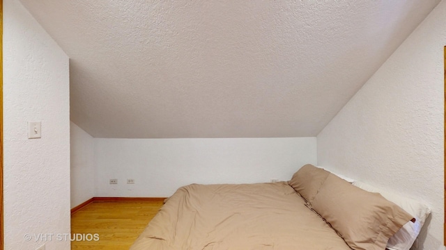 bedroom featuring lofted ceiling, a textured ceiling, baseboards, and wood finished floors