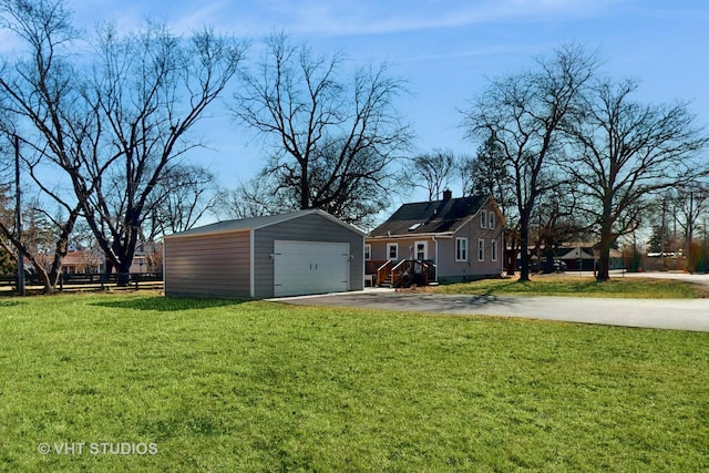 exterior space with driveway, a lawn, a detached garage, a chimney, and an outbuilding