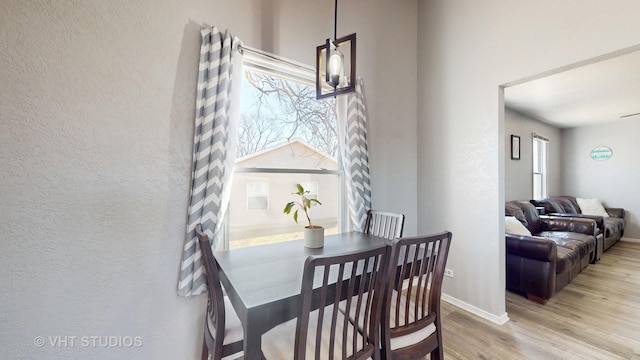 dining space featuring a textured wall, light wood-style flooring, and baseboards