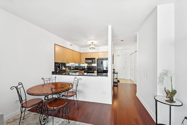 kitchen with baseboards, dark wood finished floors, dark countertops, a peninsula, and black appliances