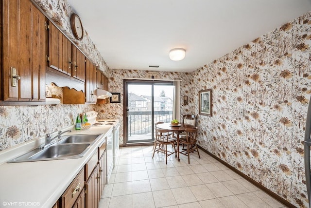 kitchen featuring wallpapered walls, white range with electric cooktop, brown cabinetry, and a sink