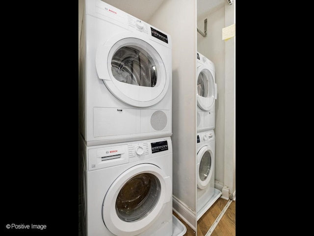 clothes washing area with stacked washer and dryer, baseboards, and wood finished floors