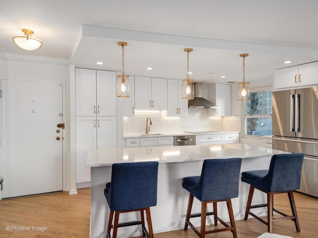 kitchen with white cabinets, a center island, hanging light fixtures, freestanding refrigerator, and wall chimney range hood