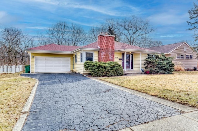 single story home featuring aphalt driveway, a chimney, a front yard, and fence