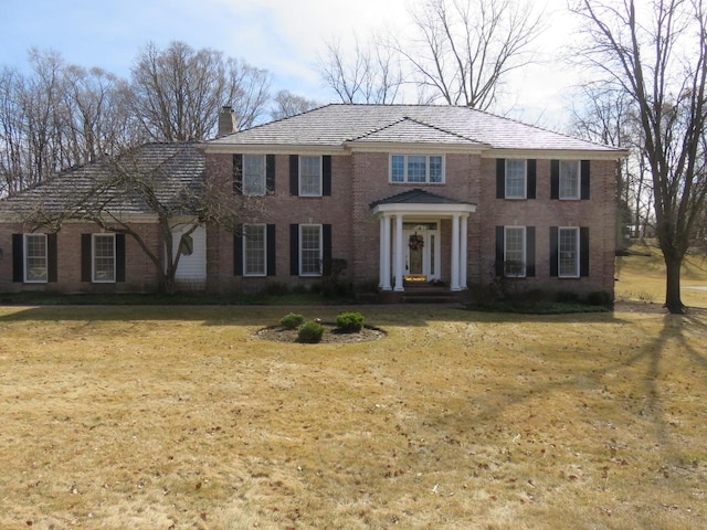 view of front of house featuring brick siding, a chimney, and a front lawn