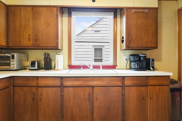 kitchen featuring brown cabinets, a toaster, light countertops, and a sink