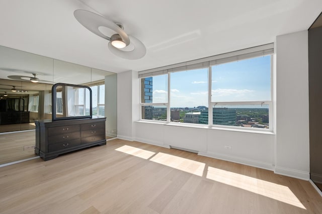 unfurnished bedroom with light wood-style floors, ceiling fan, a view of city, and baseboards