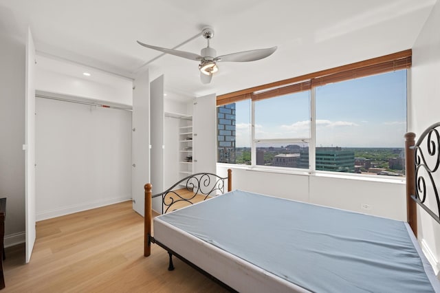 bedroom featuring baseboards, a ceiling fan, a city view, light wood-type flooring, and a closet