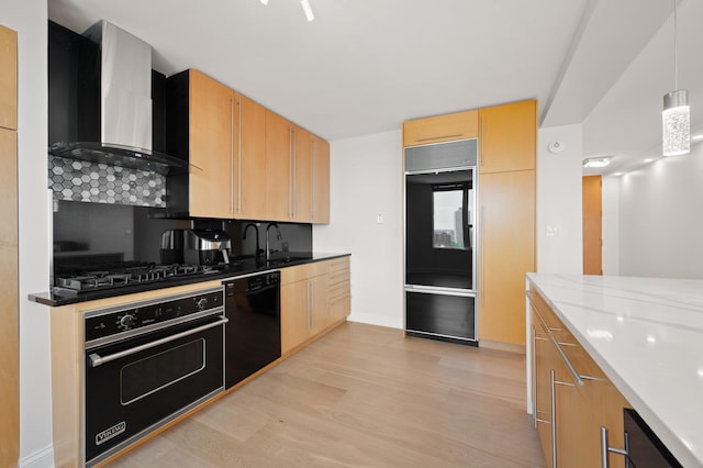 kitchen with pendant lighting, light wood-style floors, a sink, wall chimney range hood, and black appliances