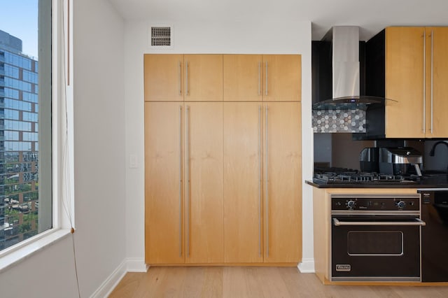 kitchen with black appliances, wall chimney range hood, visible vents, and light brown cabinetry