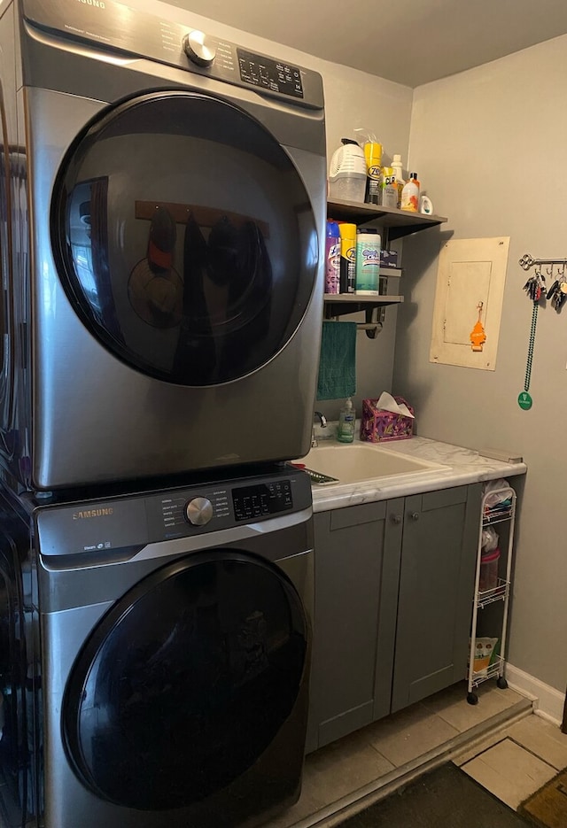 laundry room with light tile patterned floors, cabinet space, stacked washer / dryer, a sink, and baseboards