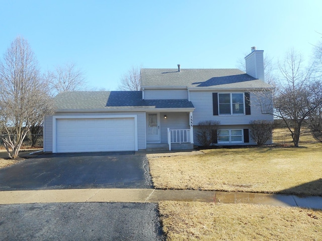 tri-level home featuring a garage, a shingled roof, a chimney, aphalt driveway, and a front lawn