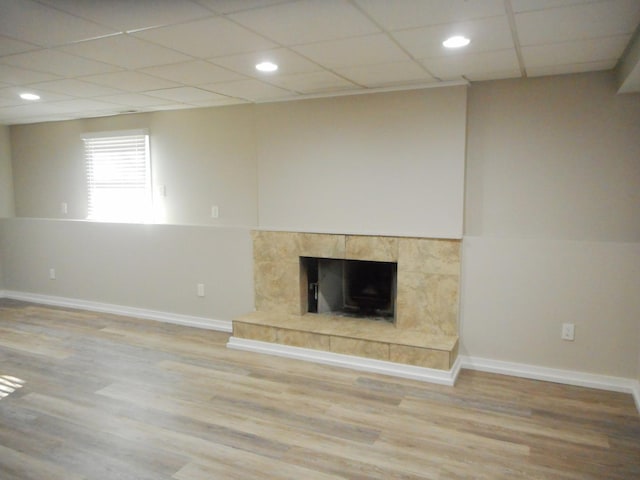 unfurnished living room featuring a paneled ceiling, baseboards, a tiled fireplace, and wood finished floors