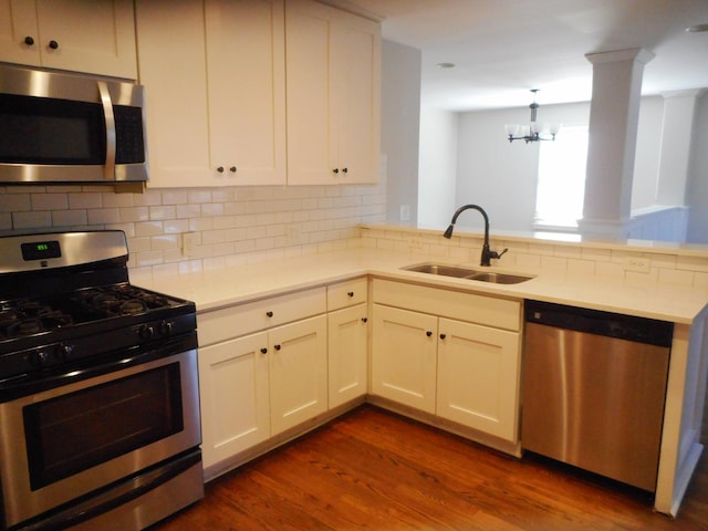 kitchen featuring a peninsula, a sink, appliances with stainless steel finishes, decorative backsplash, and dark wood finished floors