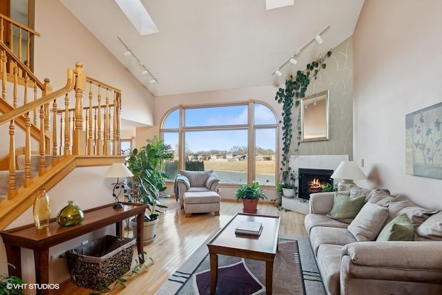 living area featuring stairs, a skylight, a large fireplace, and wood finished floors