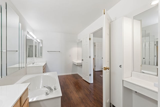 bathroom with wood finished floors, baseboards, two vanities, a sink, and a garden tub